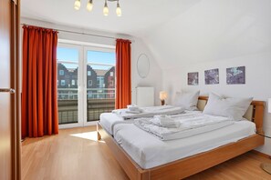 Habitación de hotel con una cama grande, dos mesitas de noche, una ventana con cortinas, un radiador y una obra de arte en la pared.