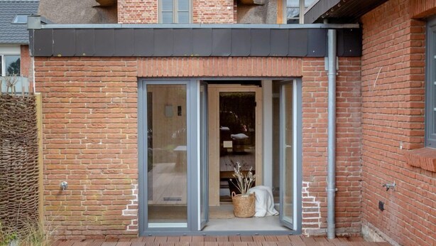 Una casa moderna con facciata in mattoni, tetto di paglia e terrazza in legno, decorata con verdure fresche e fiori.