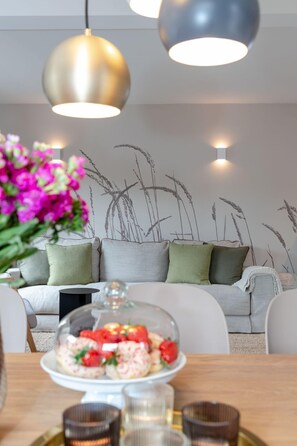 Un espace de repas moderne avec une table mise pour le repas, un canapé avec des coussins et des œuvres d’art décoratives au mur.