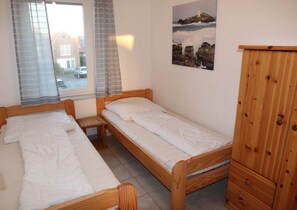 Ein Zimmer mit zwei Holzbetten, einem kleinen Holztisch, einem Schrank aus Holz, einem Fenster mit Vorhängen und einem Bild an der Wand.