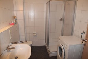 Ein Badezimmer mit Waschbecken, Toilette, Dusche und Waschmaschine.