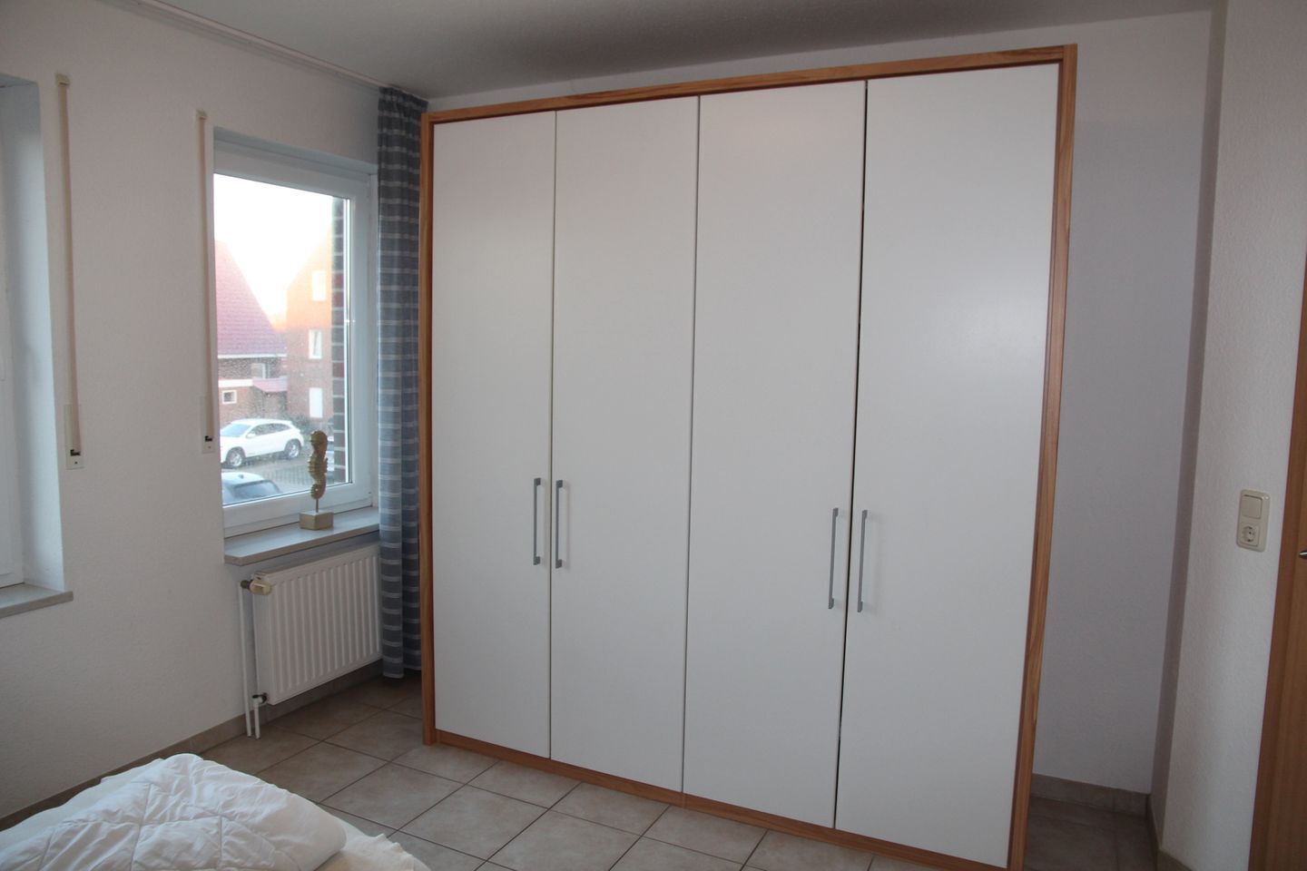 Een slaapkamer met een grote garderobe, een raam met uitzicht op een geparkeerde auto en een radiator.