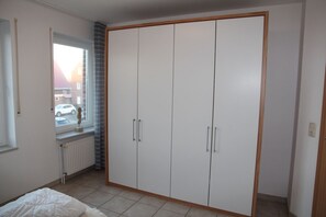 A bedroom with a large wardrobe, a window with a view of a parked car, and a radiator. - Lighthouse - vacation apartment (60sqm) for 4 persons and dog with balcony in (Norden)