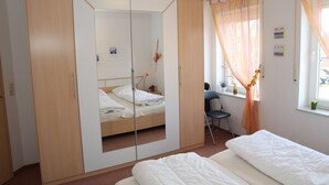 Ein Schlafzimmer mit Bett, Kleiderschrank, Schreibtisch und einem fensterbepflanzten Fenster.