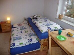 A small, tidy room with two beds, a wooden table with a green tray, and a window with a view of buildings.
