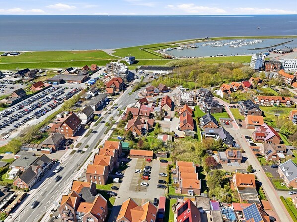 Vista aérea de un pueblo costero con edificios residenciales, un puerto deportivo y un amplio estacionamiento.