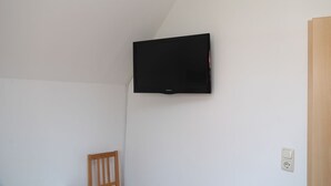 Ein Zimmer mit an der Wand befestigtem Fernseher, einem Holzstuhl und einer Tür.