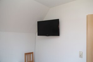 Ein Zimmer mit an der Wand befestigtem Fernseher, einem Holzstuhl und einer Tür.