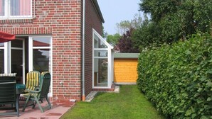 Ein Backsteinhaus mit Terrasse, einer grünen Hecke und einem Holzzaun.