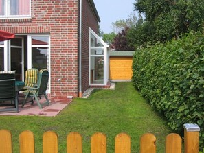 Tiilitalo, jossa on patio, vihreä pensasaita ja puinen aita.