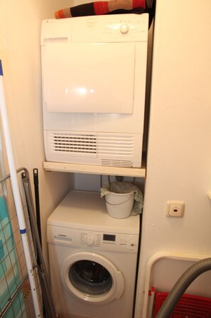 Ein Waschraum mit einer Waschmaschine mit Oberlader und einem darunter platzierten Wäschetrockner.