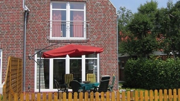 A brick house with a red awning over a patio, a window with curtains, and a wooden fence.