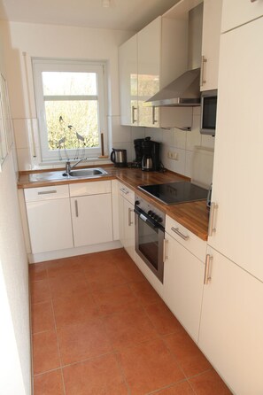 A compact kitchen with white cabinets, a wooden countertop, a built-in oven, and a window with a view of trees.