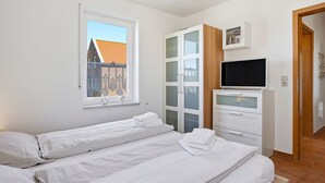 Une chambre avec deux lits, une télévision et une fenêtre donnant sur des immeubles.
