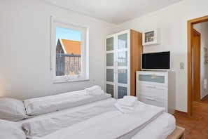 Un dormitorio con dos camas, un televisor y una ventana con vista a edificios.