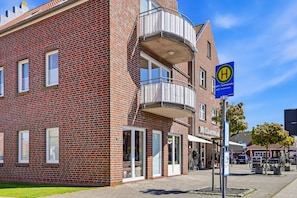 En byggnad med fasad av rött tegel, en balkong i ett av hörnen, en butiksfasad med namnet ”My Coastwear” och en blå skylt som visar var busshållplatsen ligger.