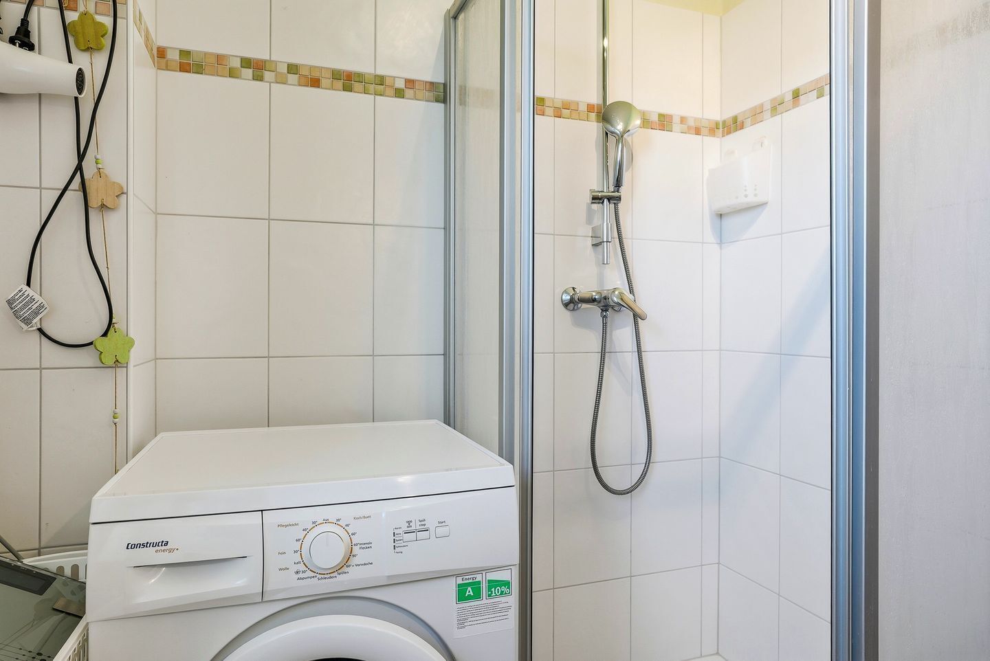 A compact bathroom with a washing machine, a shower with a handheld hose, and tiled walls.