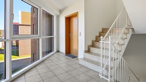 Une pièce spacieuse avec de grandes fenêtres, un escalier et une porte donnant sur un autre espace.