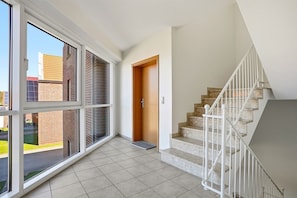 Amplia habitación con ventanas grandes, una escalera y un acceso a otra zona.