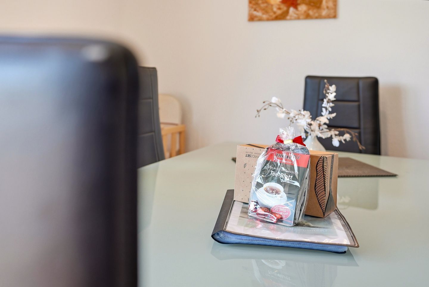 Una mesa de vidrio con un regalo envuelto, una silla negra y un cuadro en la pared.
