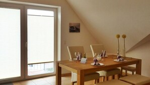 A dining area with a wooden table, chairs, and a sliding glass door leading to an outdoor balcony. - Juistblick - Beautiful top floor apartment (60sqm) for 4 persons with balcony and (Norden)