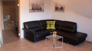 A living room with a black leather sofa, a glass coffee table with candles, and two framed pictures on the wall. - Juistblick - Beautiful top floor apartment (60sqm) for 4 persons with balcony and (Norden)