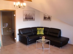 Un salon avec un canapé en cuir noir, une table basse en verre ornée de bougies et deux tableaux encadrés accrochés au mur.