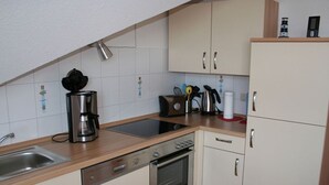 A kitchen with a dishwasher, stove, and coffee maker. - Möwennest - Beautiful vacation apartment (60sqm) for 4 persons and dog with balcony in (Norden)