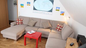 A living room with a sofa, a red table, and a television. - Möwennest - Beautiful vacation apartment (60sqm) for 4 persons and dog with balcony in (Norden)