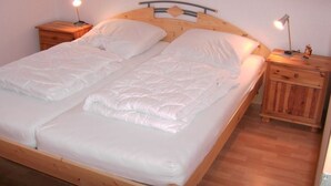 A double bed with a wooden frame and headboard, two bedside tables with lamps, and a wooden floor. - Möwennest - Beautiful vacation apartment (60sqm) for 4 persons and dog with balcony in (Norden)