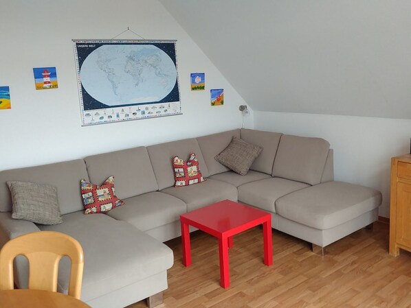 A cozy living room with a large sofa, a red table, and a world map on the wall.