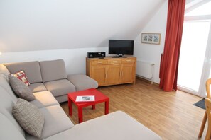 Un salon moderne avec un canapé, une table basse rouge, un meuble en bois, un téléviseur et une fenêtre avec des rideaux.