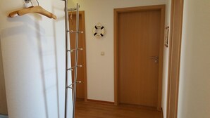 Un pasillo con una puerta de madera, un círculo salvavidas colgado en la pared y un perchero.