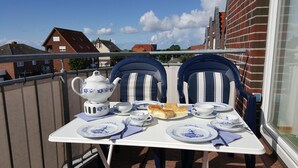 Un balcón con una mesa dispuesta para el té, dos sillas y vistas a edificios.
