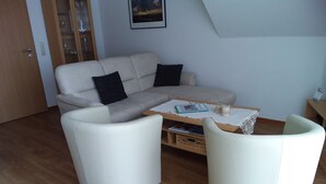 Una sala de estar moderna con un sofá, dos sillones blancos, una mesita de centro y una estantería.