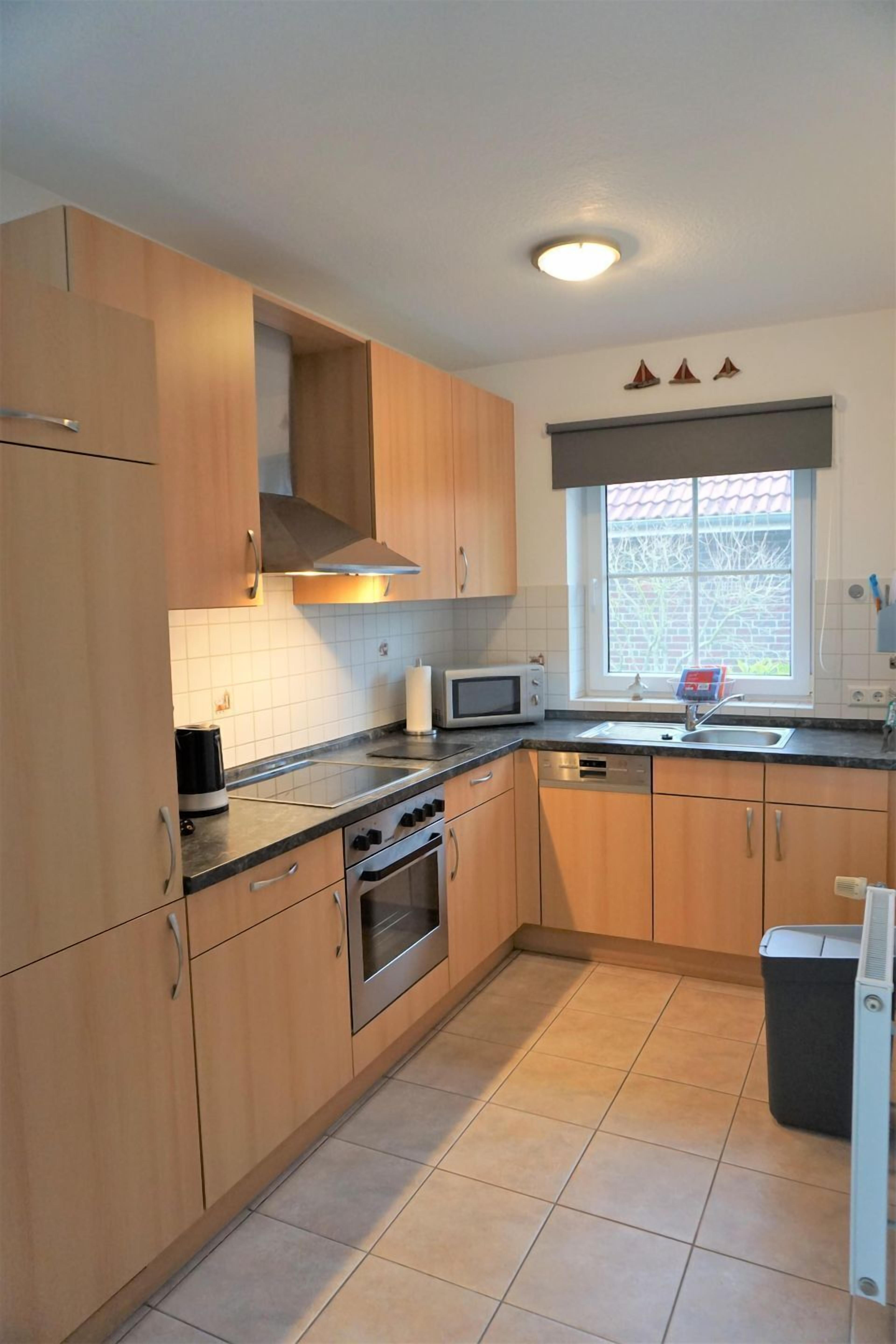 Een keuken met houten kastjes, een magnetron, een oven, een spoelbak en een raam met uitzicht.