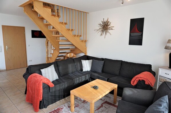 A living room with a black leather sofa, a wooden coffee table, a wooden staircase, and a wall with a star decoration and a red bridge painting.