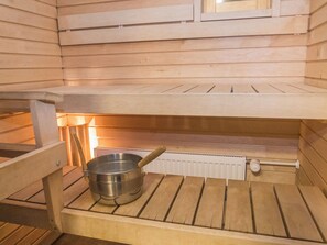 Uma sauna com banco de madeira, bacia de metal e radiador.
