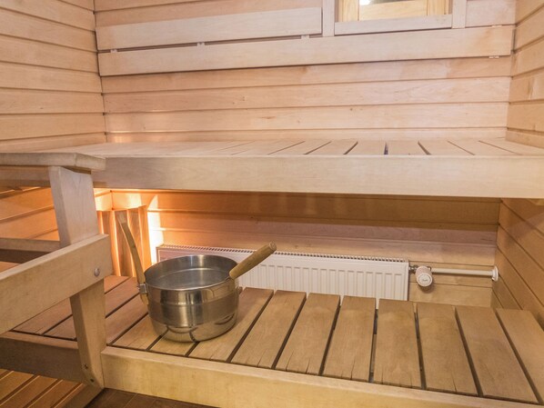 Sauna, jossa on puinen penkki, metallinen pesuallas ja patteri.