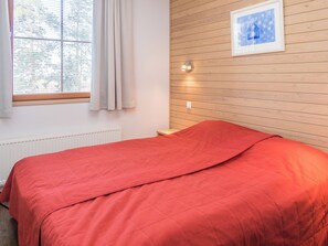 A bedroom with a bed, a window with curtains, a wall-mounted light, and a framed picture.
