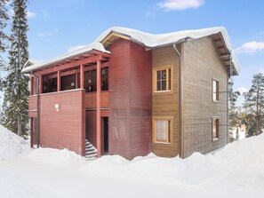 A two-story building with a red and brown exterior, a covered entrance, and a snow-covered roof.