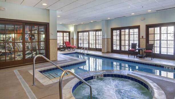 Une piscine avec un jacuzzi, des chaises longues et une vue sur l’extérieur grâce à de grandes fenêtres.