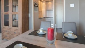 Un comedor con una mesa dispuesta para dos personas, un mueble con puertas de cristal y una cocina al fondo.