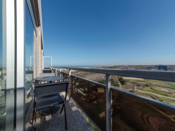 A balcony with a table and chairs, offering a view of a coastal landscape and a highway. - Astrid 902 with parking by Interhome (Bredene)
