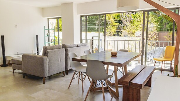 A modern living room with a sofa set, dining table, and chairs, large windows with a view of greenery, and a wooden bench. - Justo Sierra SmartLife (Guadalajara)
