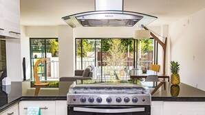 A modern kitchen with a gas stove, a stainless steel range hood, and a large window overlooking a patio area. - Justo Sierra SmartLife (Guadalajara)