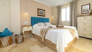 Een slaapkamer met een groot bed, een nachtkastje, een dressoir en een raam met gordijnen.