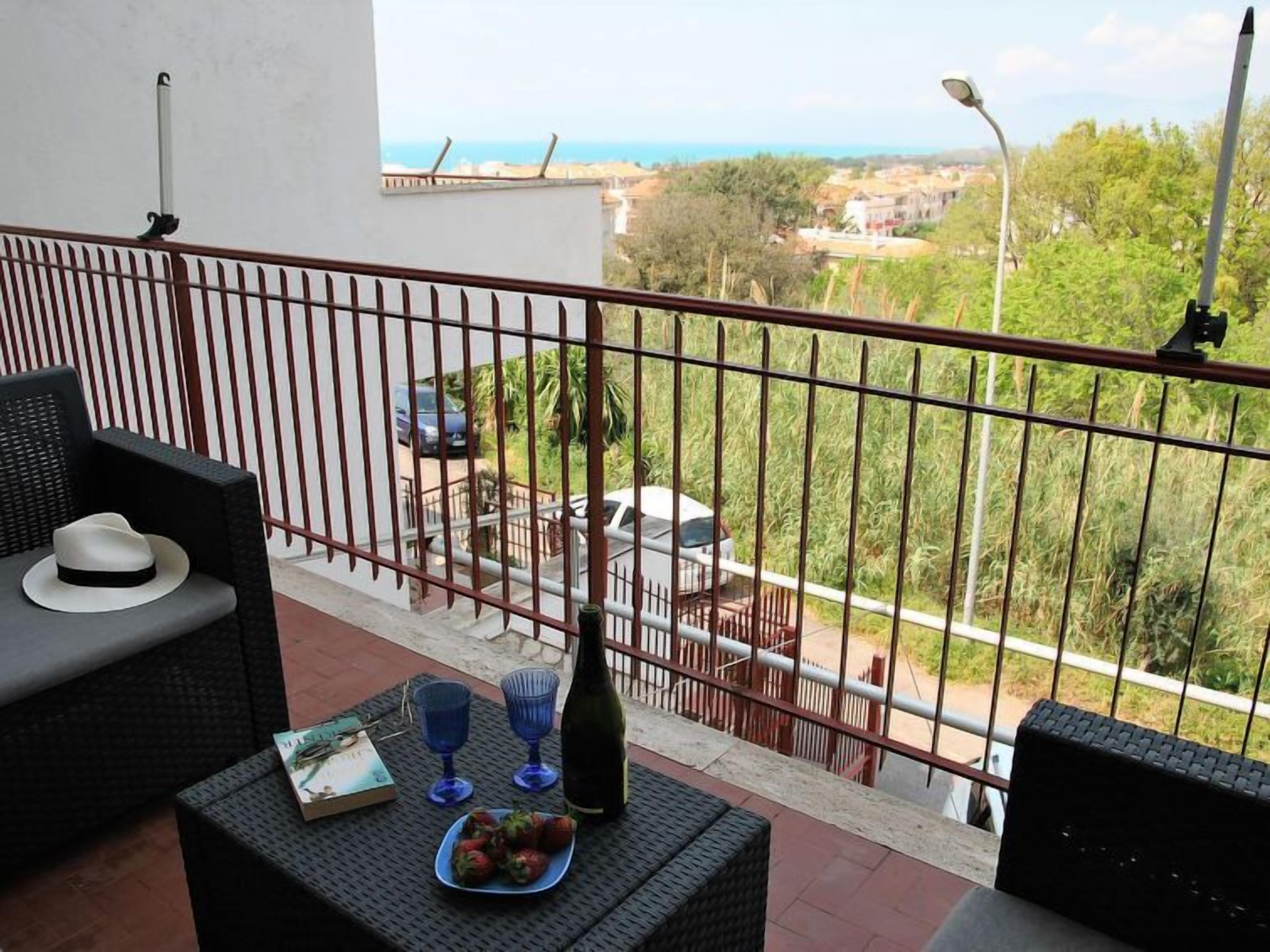 Un balcon avec des meubles en osier, une bouteille et une assiette de fraises.