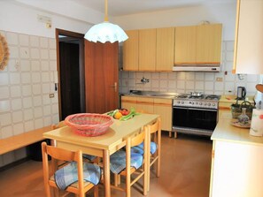 A compact kitchen with wooden cabinets, a stove, and a dining area with a table and chairs.