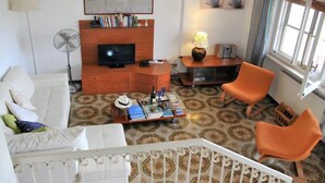 Una sala de estar con un sofá blanco, sillas anaranjadas, un televisor, un ventilador, un mapa del mundo y una lámpara.